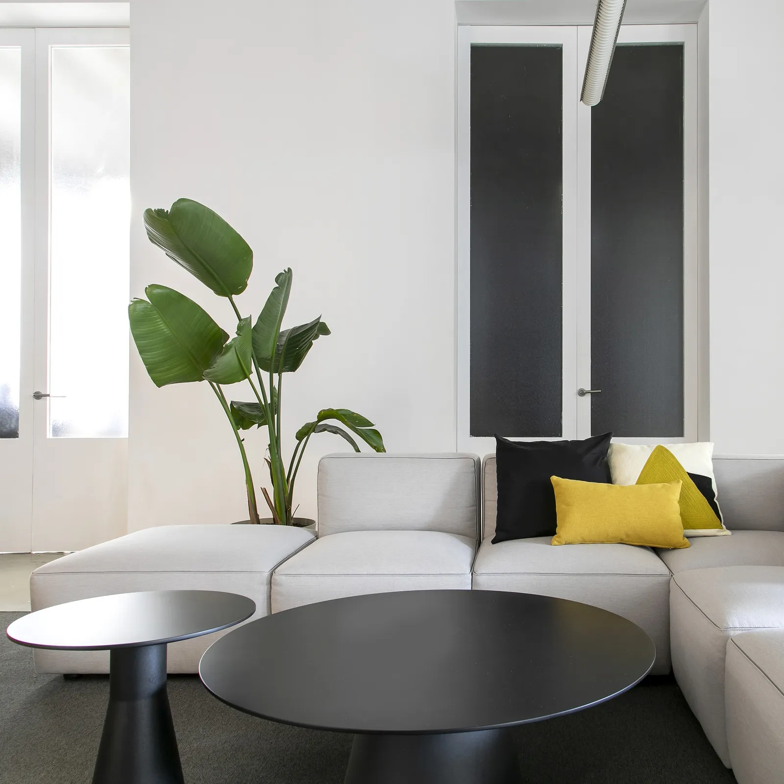 Hellgraues Dado-Sofa mit vorgelagerter Polsterfläche, gelben Kissen und schwarzen Couchtischen