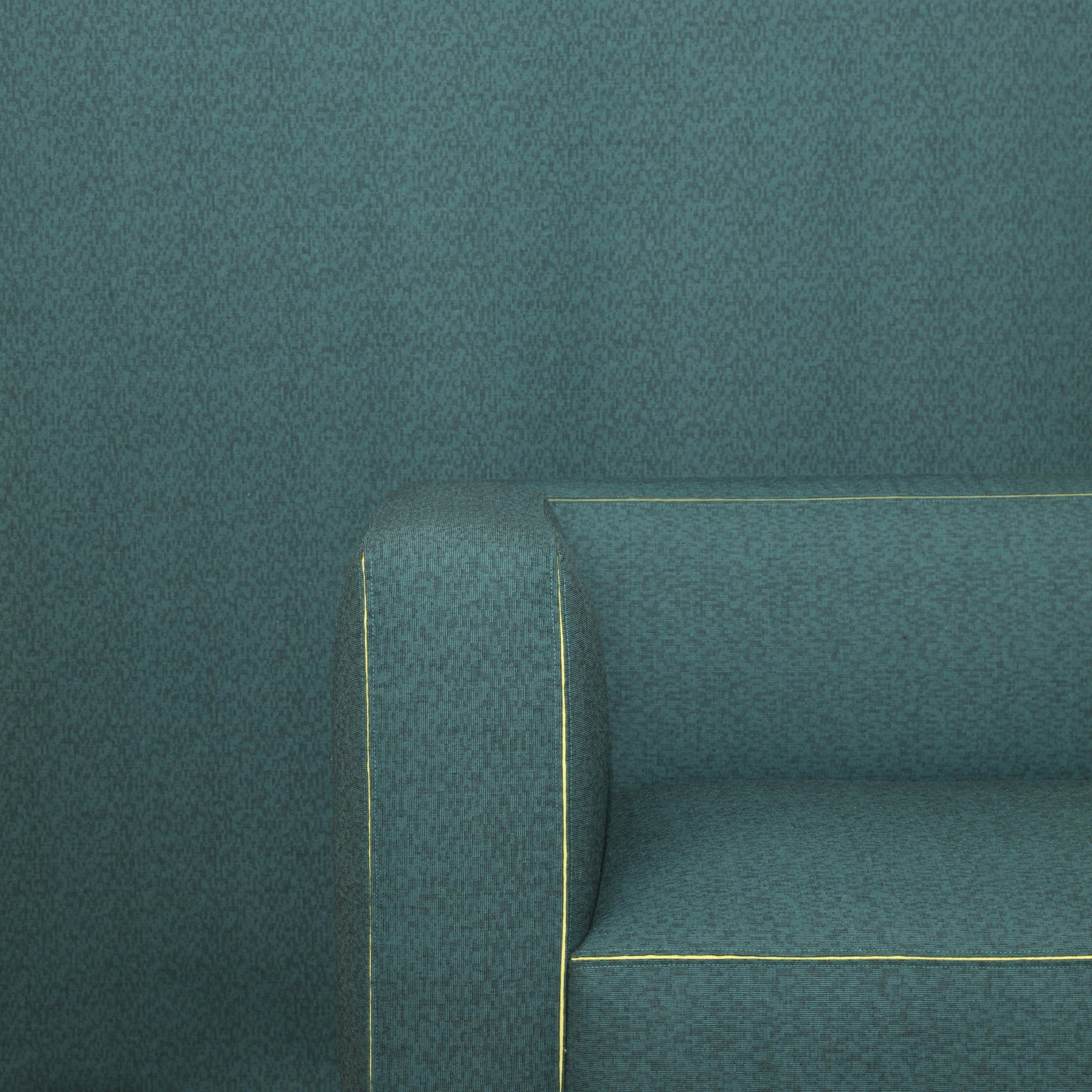 Detail des Dado-Sofas mit petrolfarbenem Stoffbezug, gepolsterter Armlehne und gelber Kontrastnaht