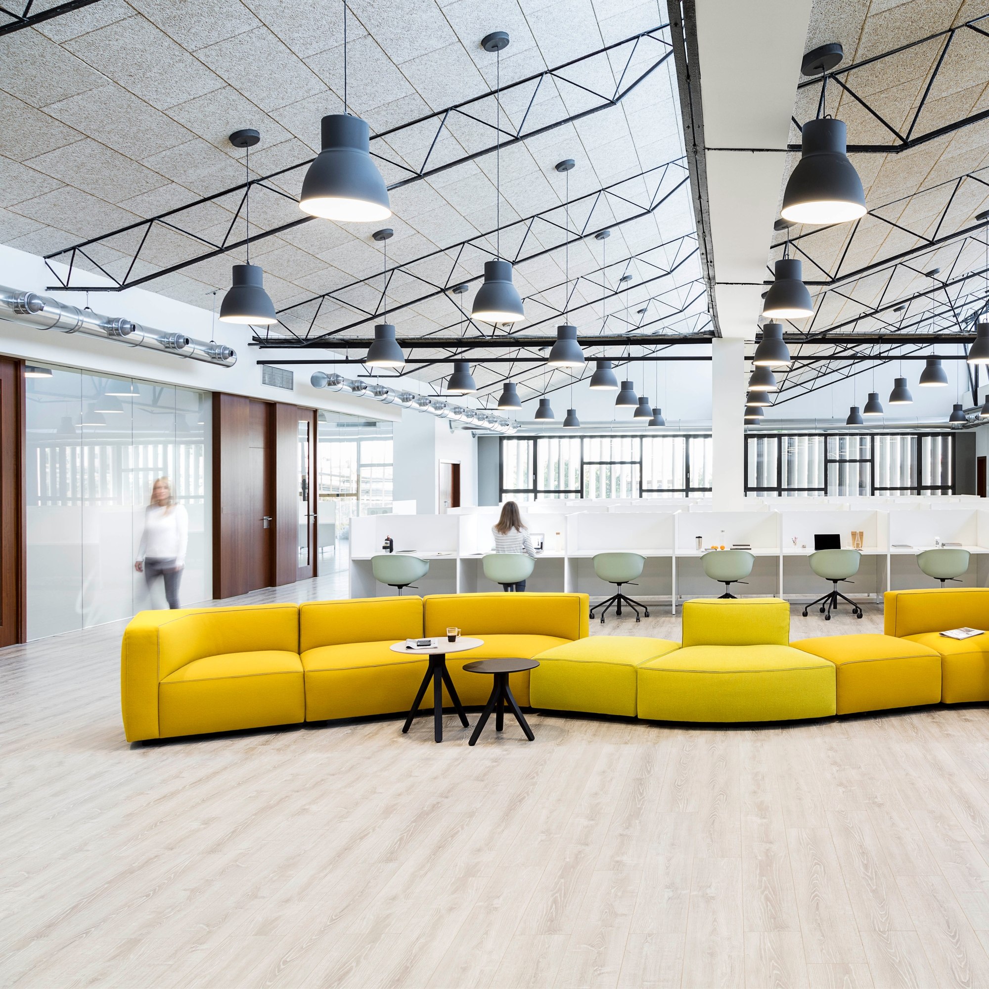 Gelbe Dado-Sofalandschaft als offene Lounge vor den Arbeitsplätzen eines hellen Büros