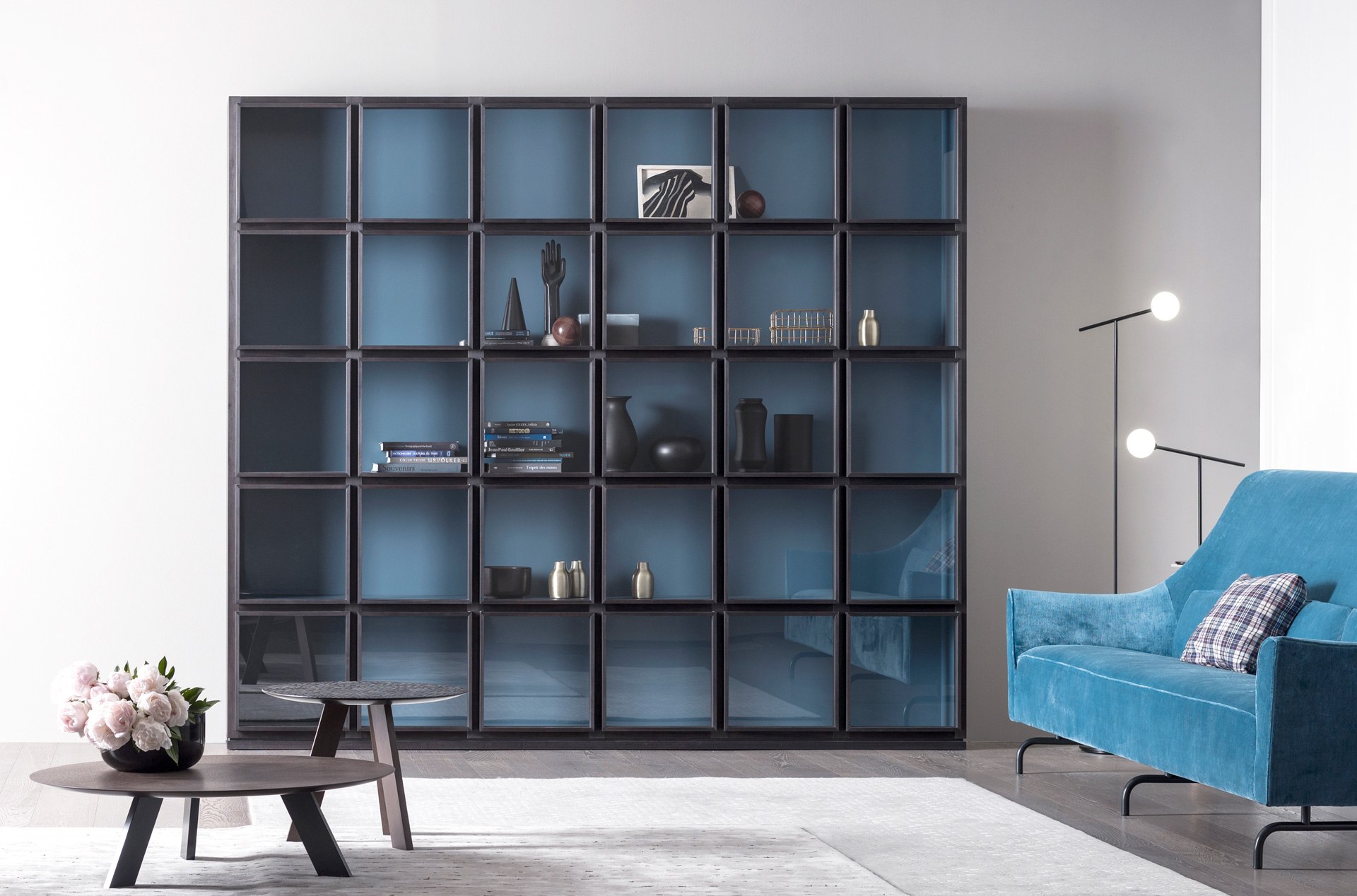 Dunkle Concept-Vitrine mit blauen Innenflächen und gerahmten Glastüren neben einem blauen Sessel.