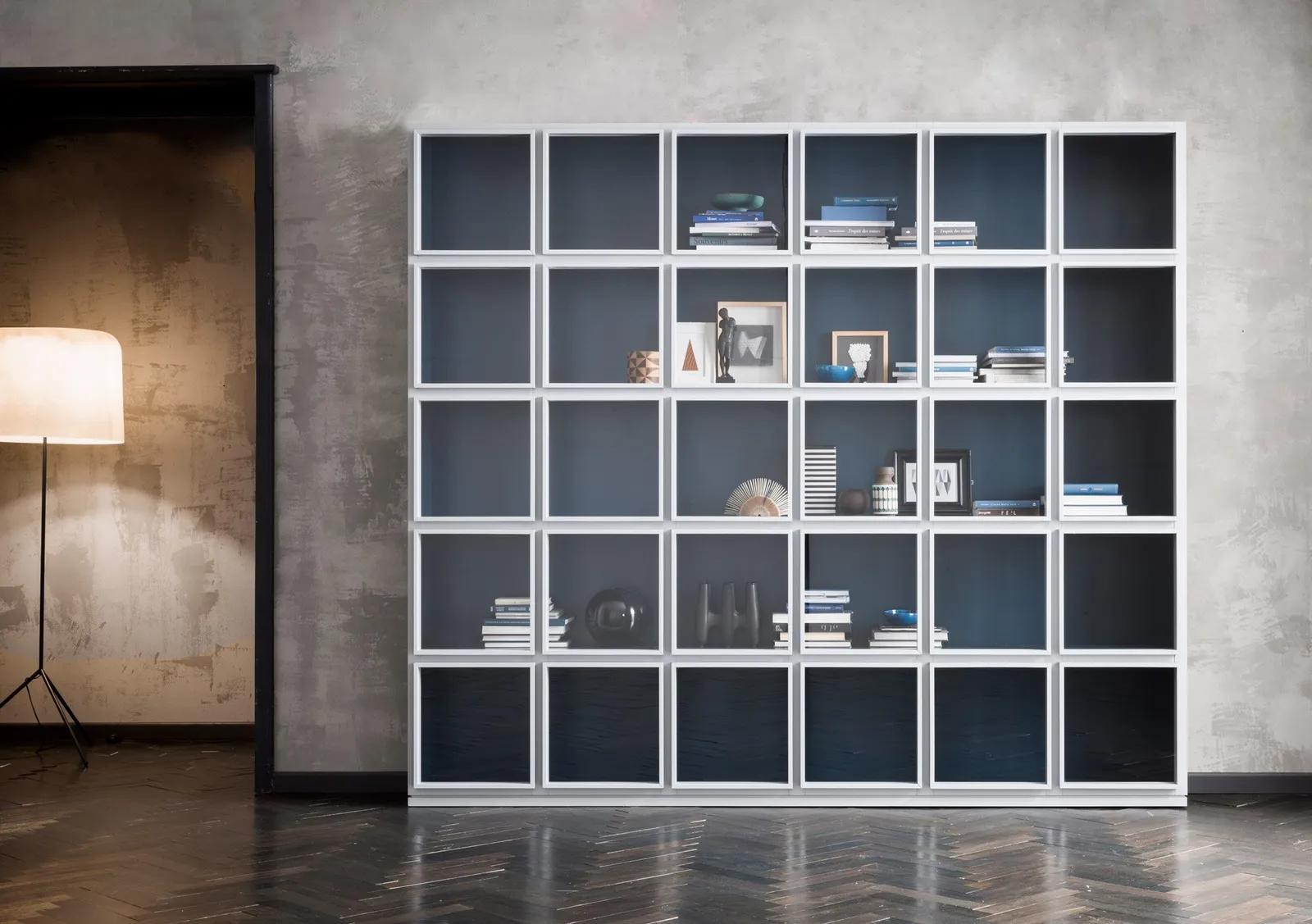 Breite Concept-Vitrine mit hellen Türrahmen, blauen Innenflächen sowie Büchern und ausgestellten Objekten.
