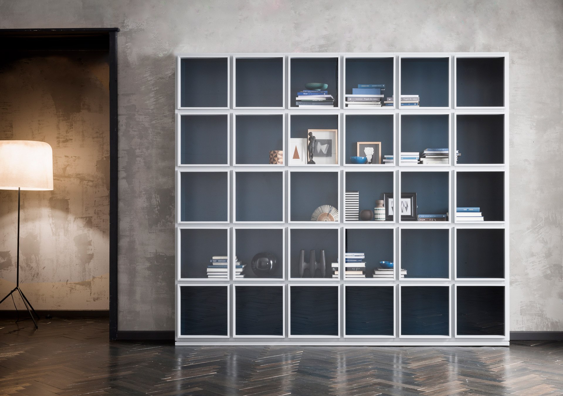 Breite Concept-Vitrine mit hellen Türrahmen, blauen Innenflächen sowie Büchern und ausgestellten Objekten.