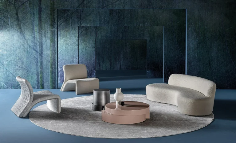 Casamilano Curvy Mono: helles geschwungenes Sofa mit Sesseln und Couchtischen vor blauer Wand