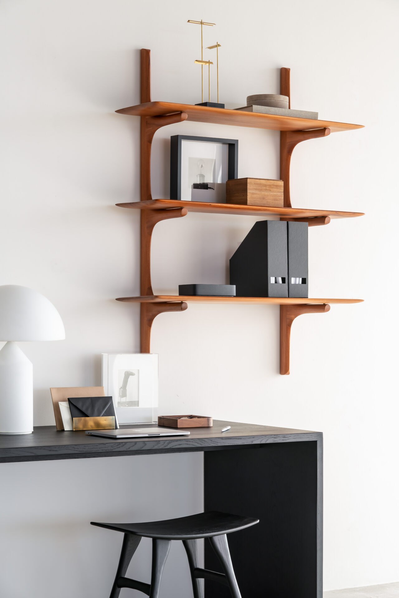 PI Wandregal mit drei Böden über einem schwarzen Schreibtisch und einem dunklen Holzhocker.