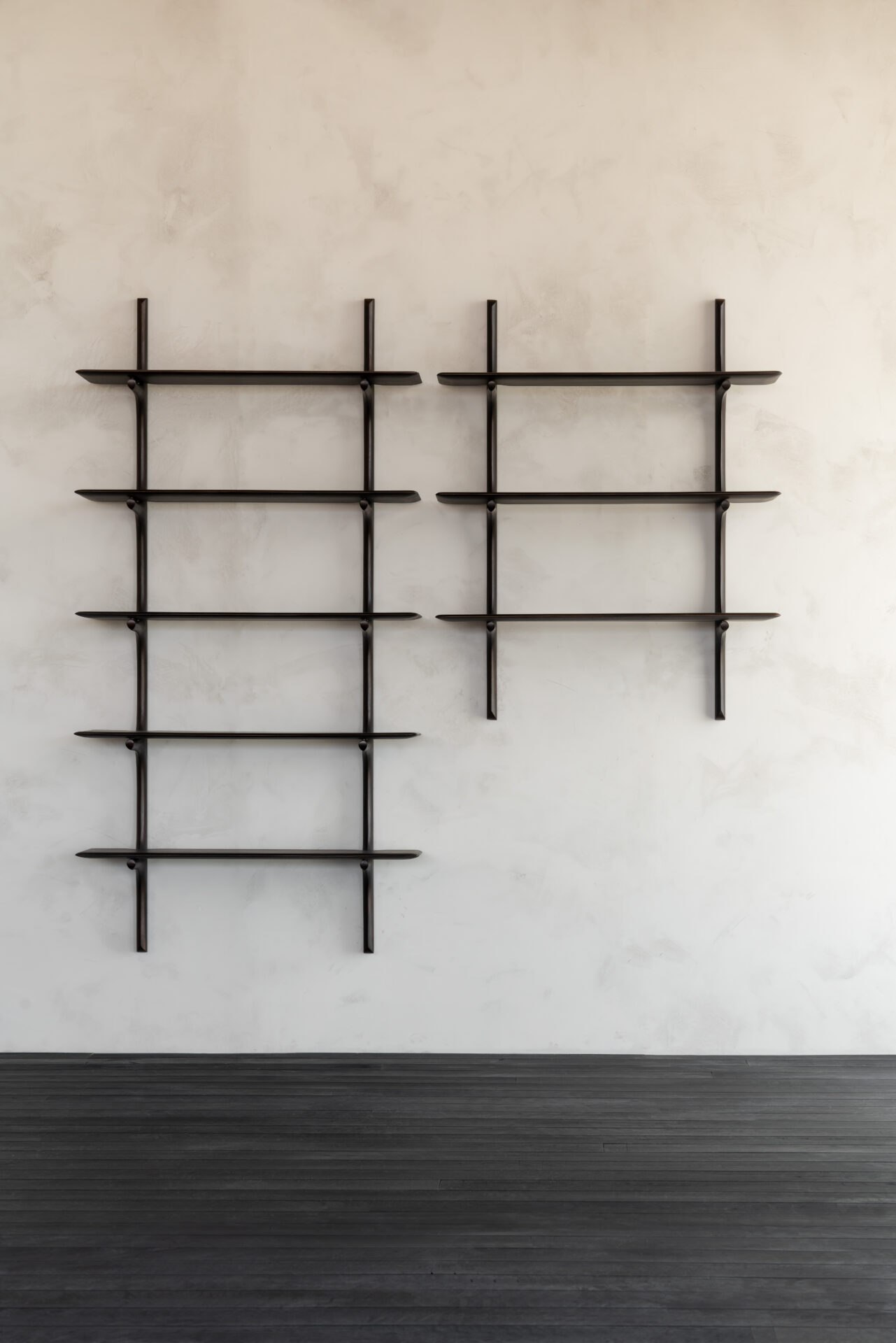 Zwei dunkle PI Wandregale mit unterschiedlich vielen Böden an einer hellen Wand, ohne Dekoration.