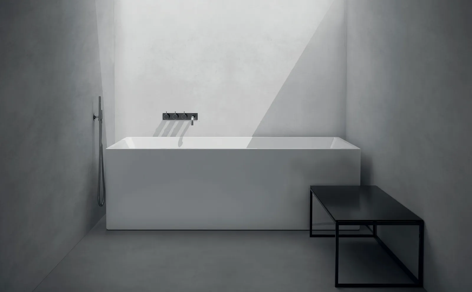 Weiße rechteckige Badewanne mit Wandarmatur und schwarzer Ablage in einem grauen Badezimmer