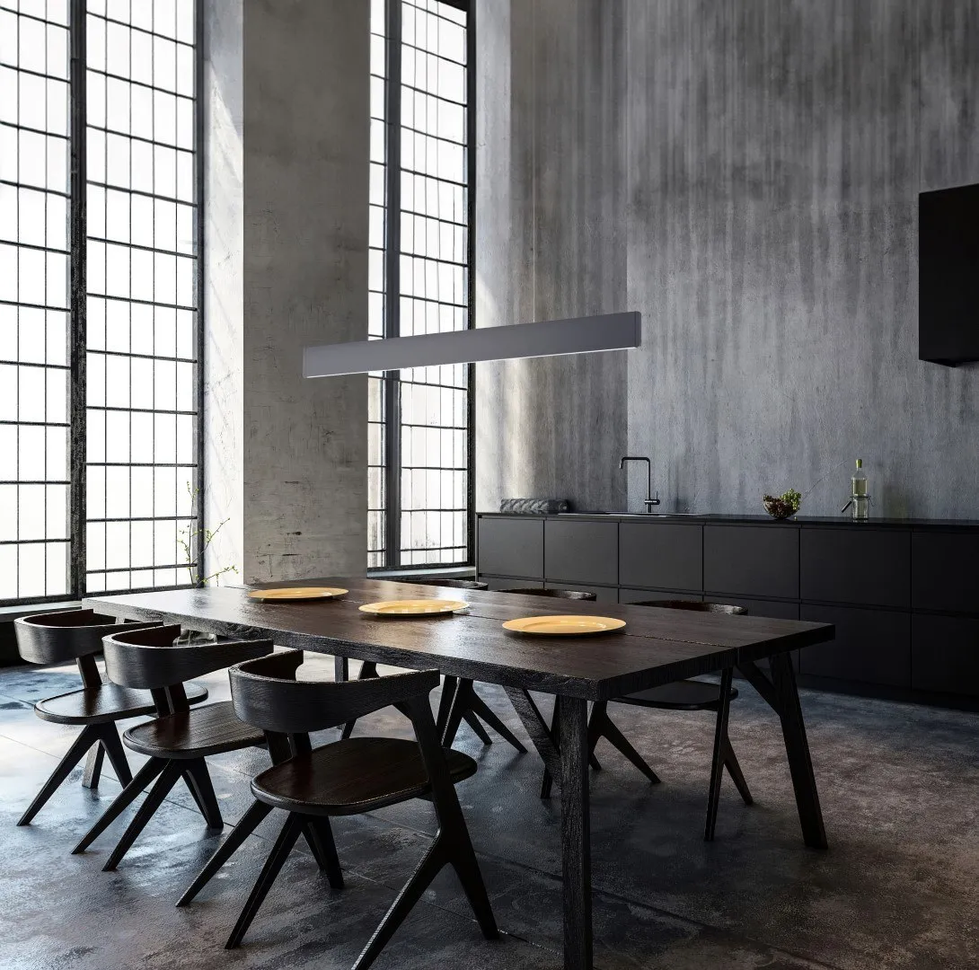 Molto Luce After8 Long: lange Pendelleuchte über einem dunklen Esstisch vor hohen Fenstern und einer Betonwand