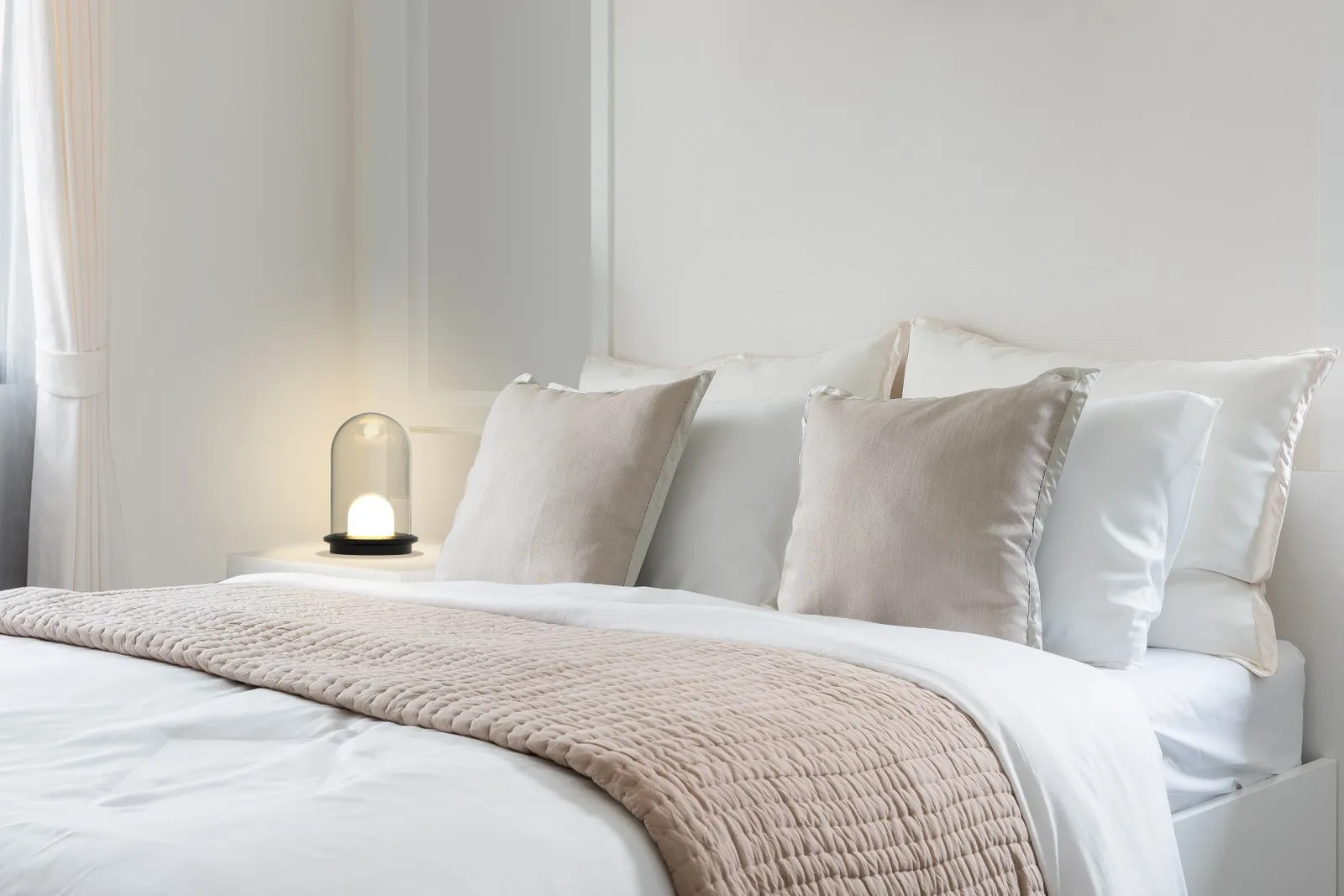 Molto Luce Pille Single: kleine Tischleuchte mit Glaskörper neben einem hell bezogenen Bett