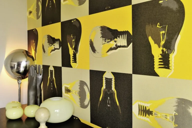 Tapete mit gelben, grauen und schwarzen Glühbirnenmotiven hinter einer Kugelleuchte und Vasen
