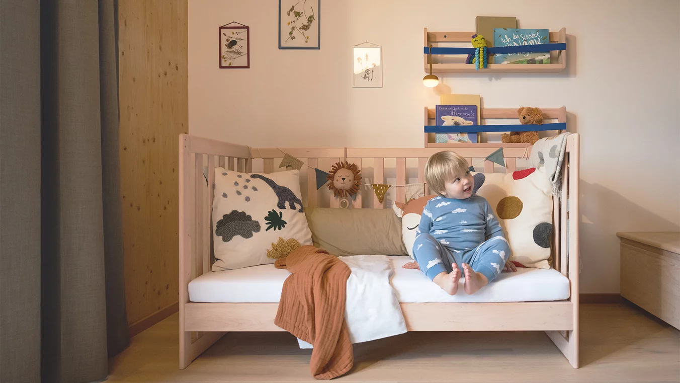 Zum Sofa umgebautes TEAM 7 kids Gitterbett aus hellem Holz mit Kind und Kissen