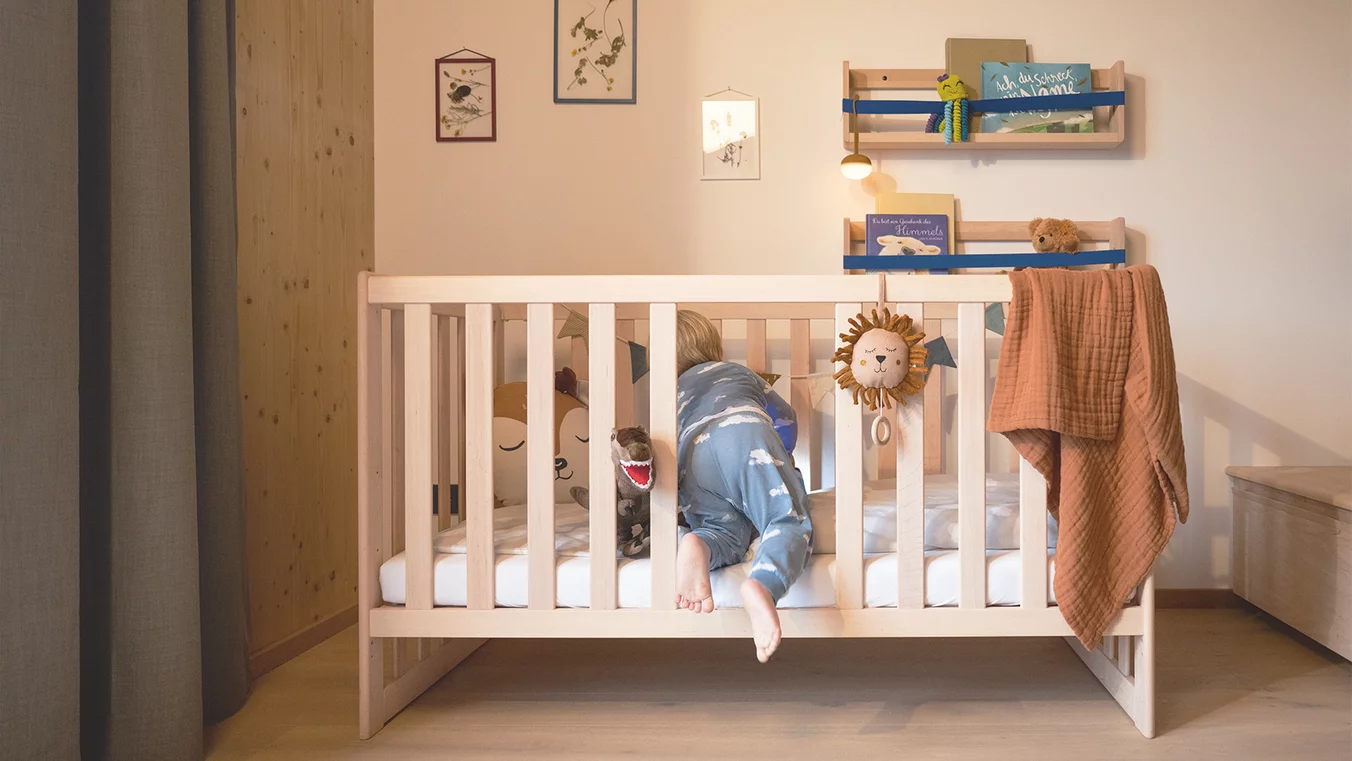Kind steigt durch die Öffnung der zwei herausgenommenen Sprossen am TEAM 7 kids Gitterbett