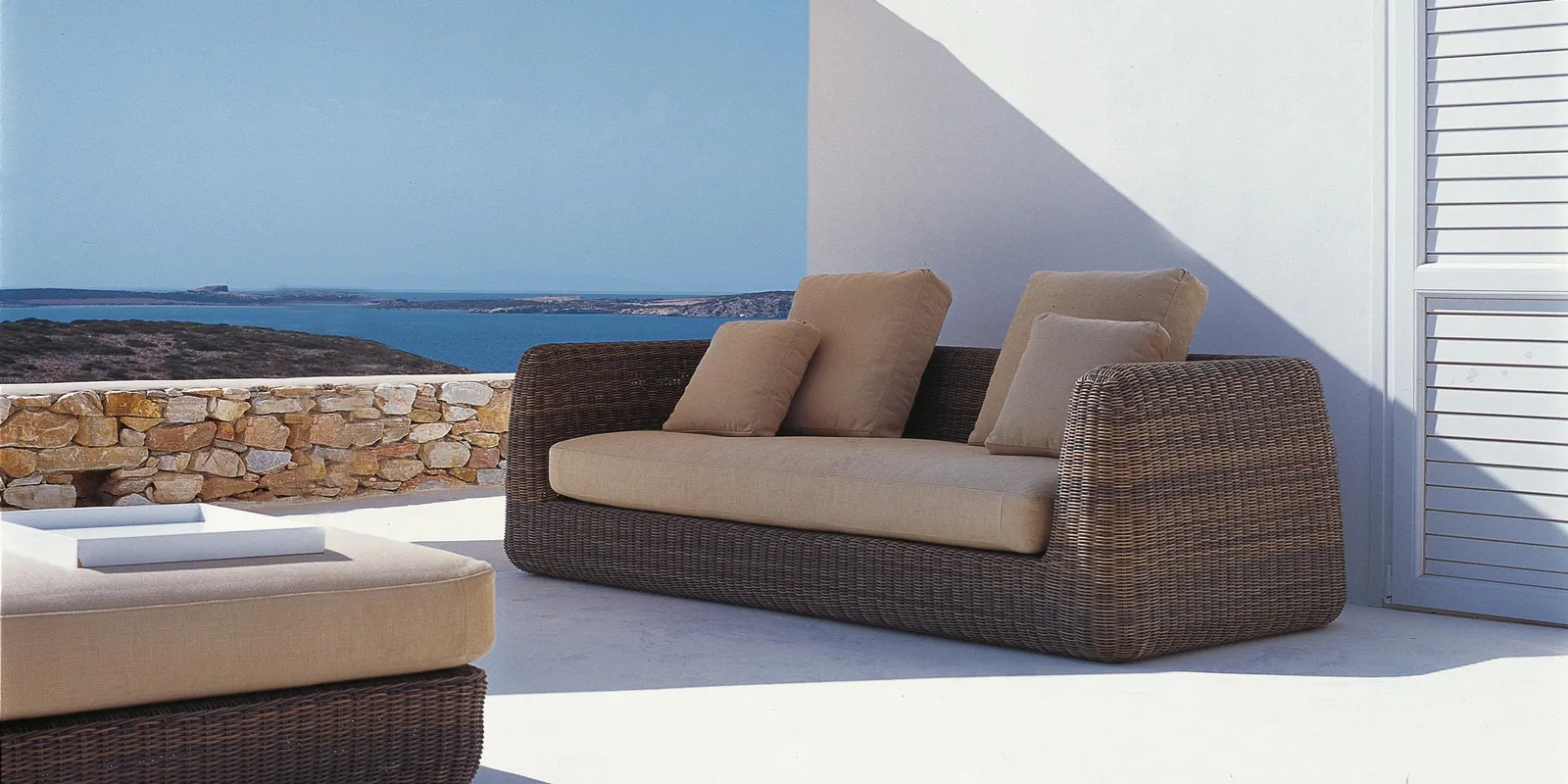 Unopiù Agorà Sofa mit braunem Geflecht und hellen Polstern auf einer Terrasse