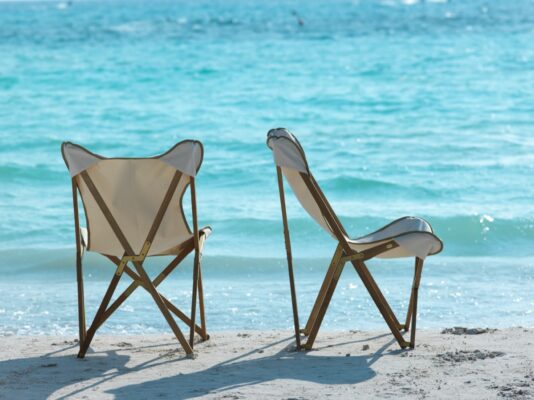 Zwei Unopiù Emy Klappsessel mit hellen Sitzbezügen am Strand, von hinten und seitlich